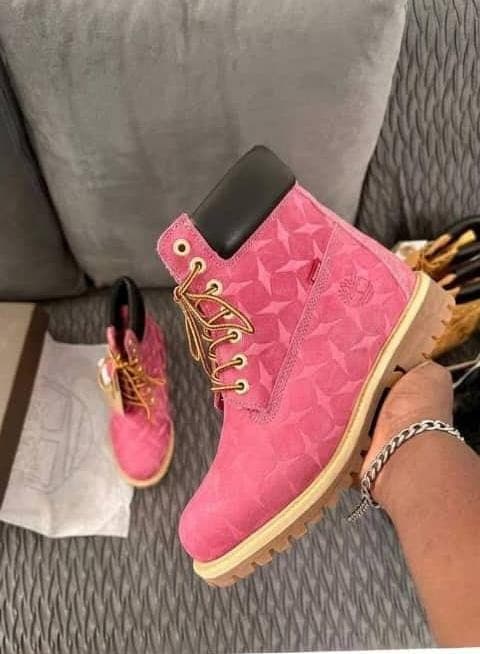 Pink geometric patterned Timberland boot with gold laces and yellow sole held in hand.