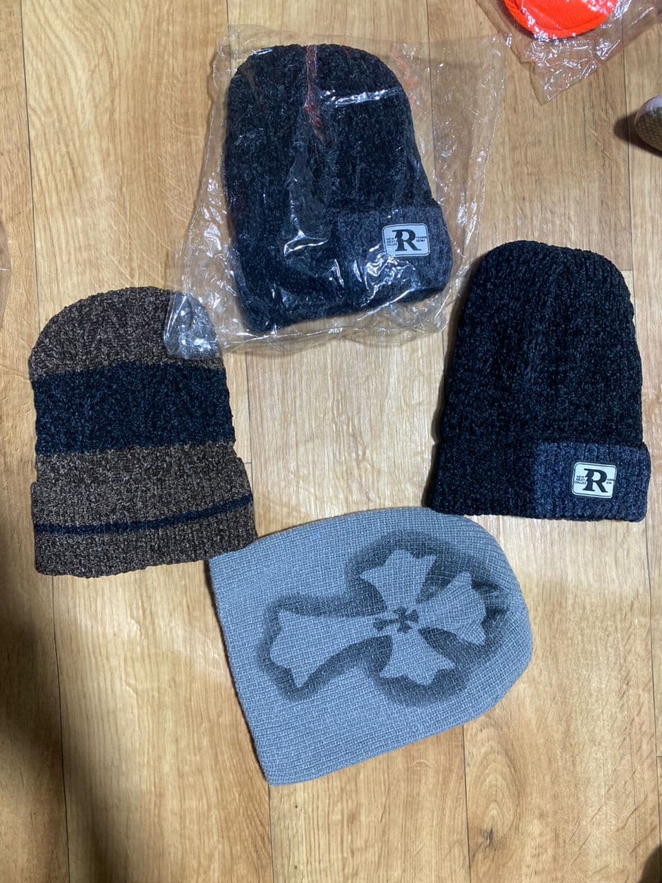 Black R logo boucle beanies, one in plastic packaging, plus striped and gray beanies on wooden floor.