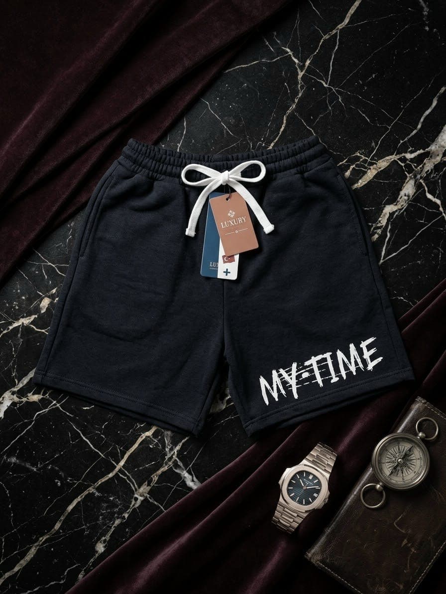 Black fleece shorts with white MY-TIME text on marble with compass and notebook props.
