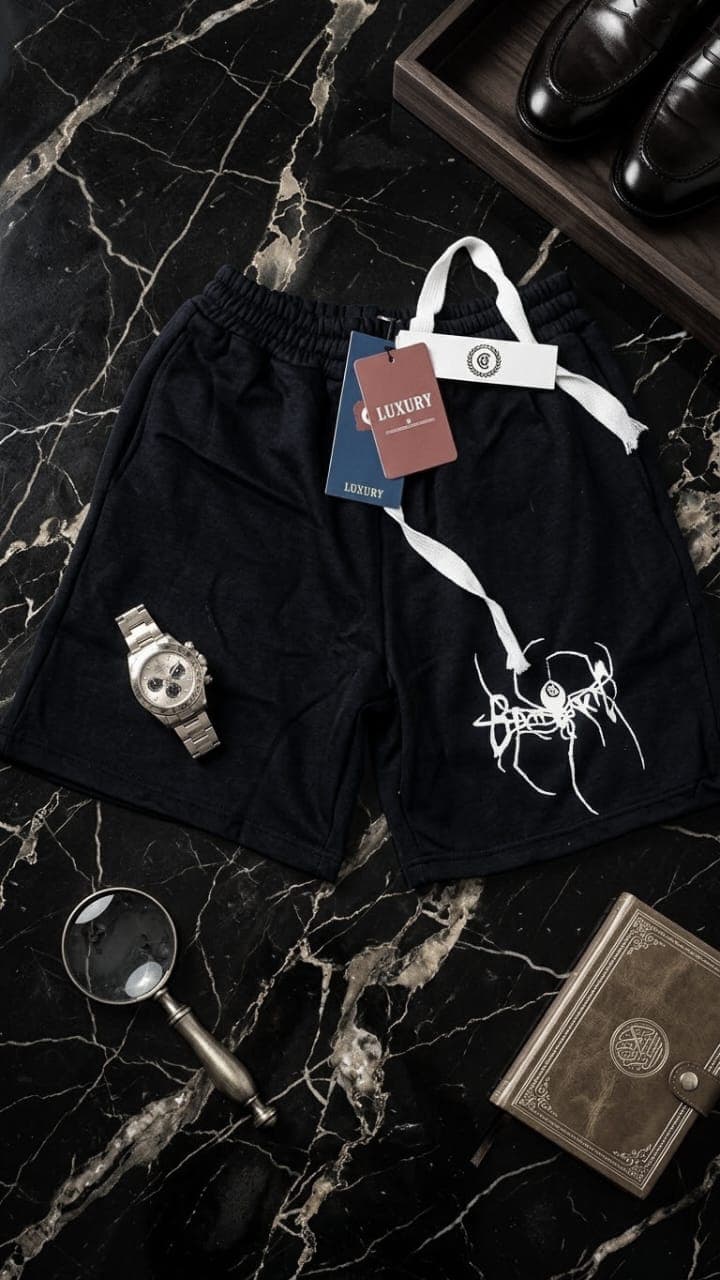 Black fleece shorts with white abstract creature graphic on marble with magnifying glass and tray.