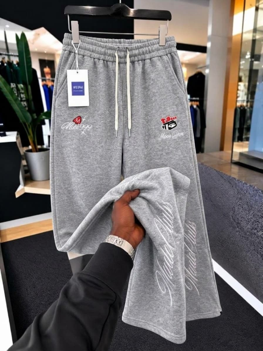 Gray Mode Gipe embroidered joggers on hanger with hand holding the leg to show details.