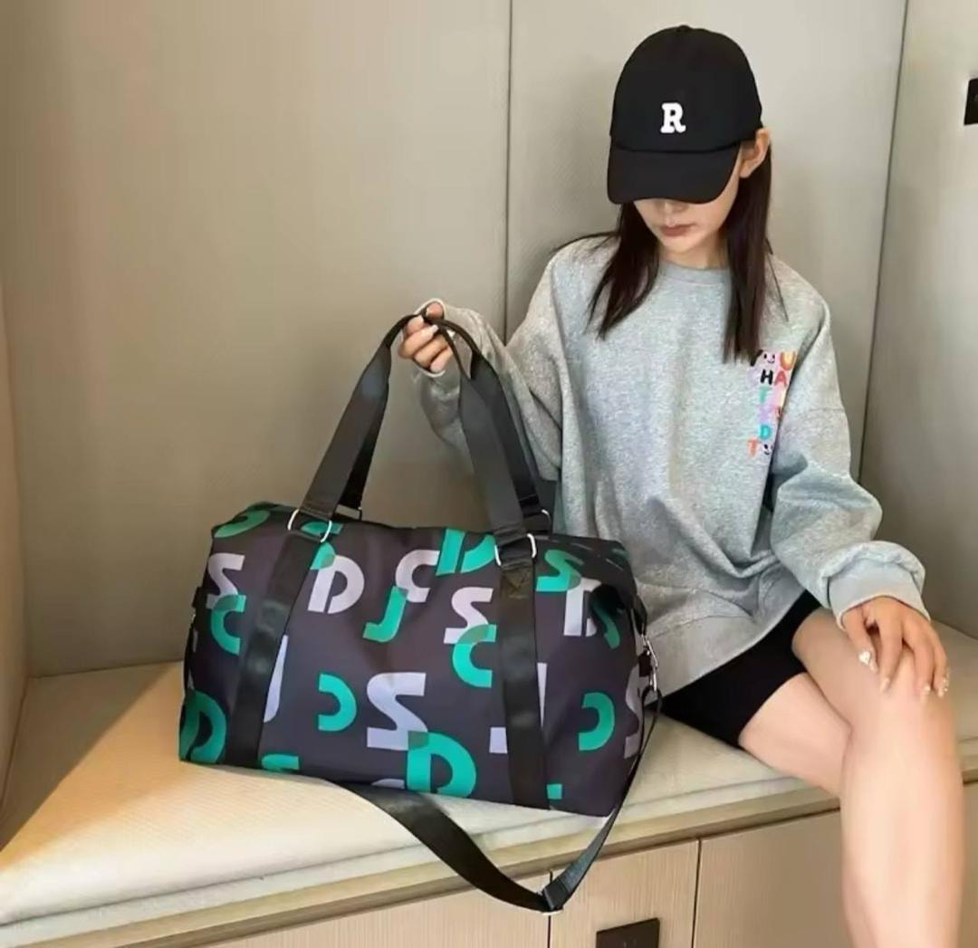 Model holding dark printed travel duffel bag with teal, white and grey lettering and black straps.