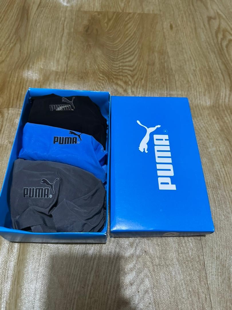 Puma 3-pack briefs in black, blue and grey inside open blue Puma box on wooden floor.