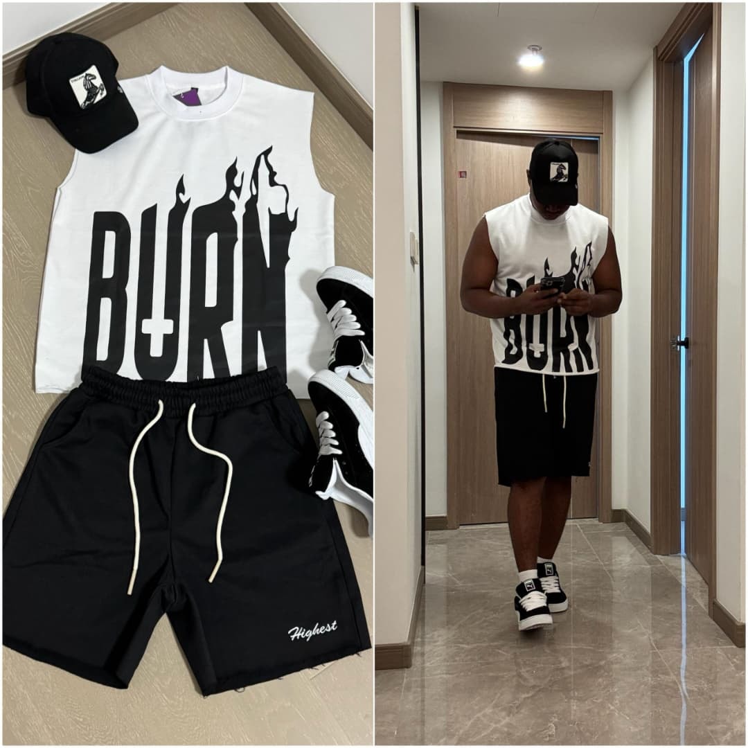 Flat lay of white sleeveless top with black BURN flame graphic, black shorts, cap and sneakers beside model wearing the black set.