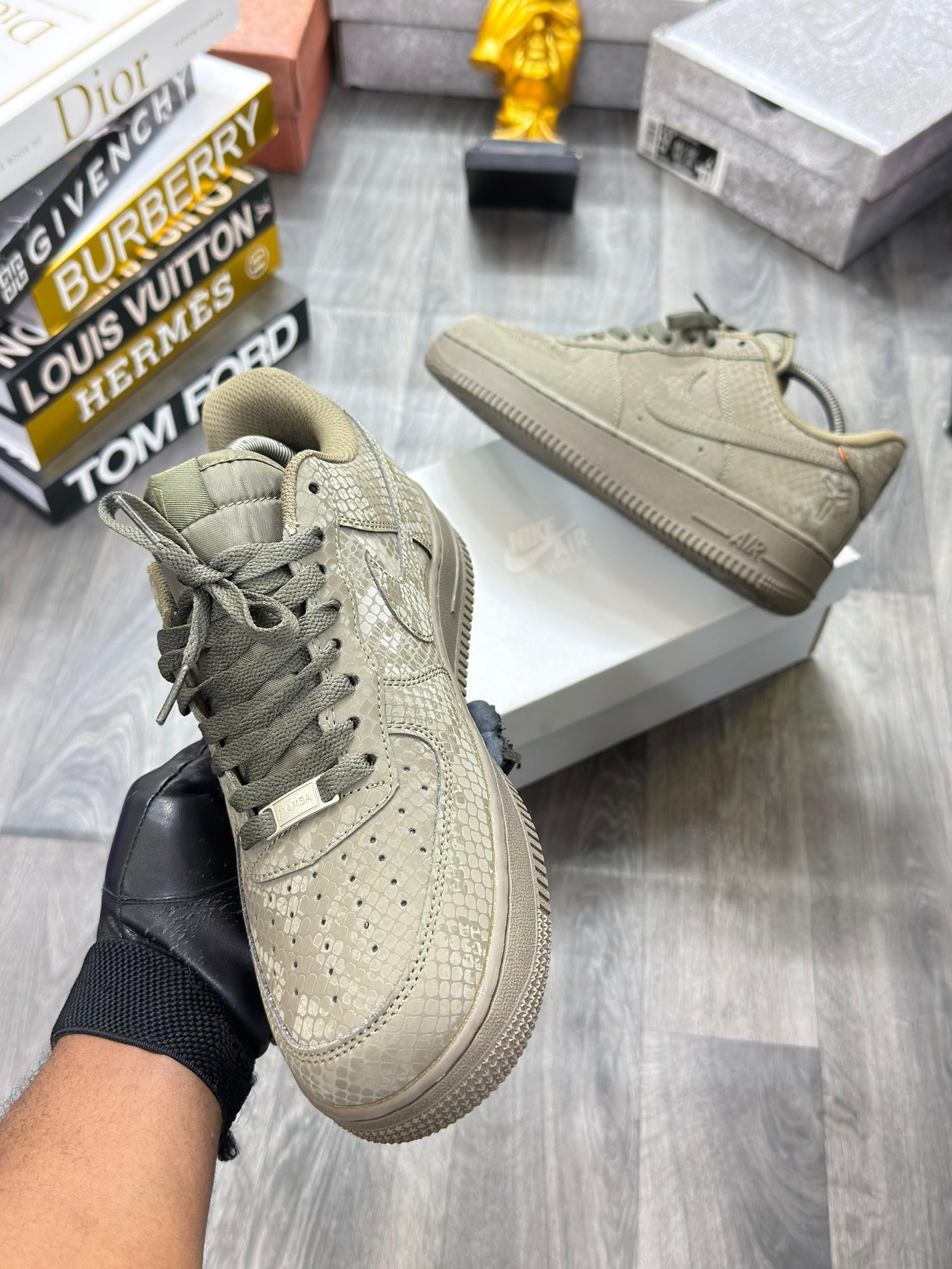 Beige snakeskin Nike Air Force 1 sneakers held in hand and shown on box with lifestyle books.
